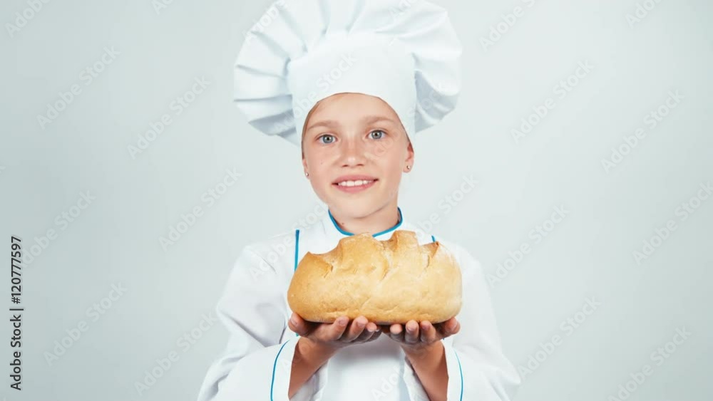 Portrait little baker sniffing bread and holds it in her hands and smiling at camera Portrait little baker sniffing bread and holds it in her hands and smiling at camera