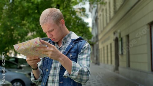 Boy looking lost while standing on pathway and reading map
