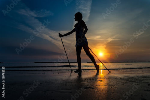 Skinny girl at sunrise on the beach to the sea with Nordic walki