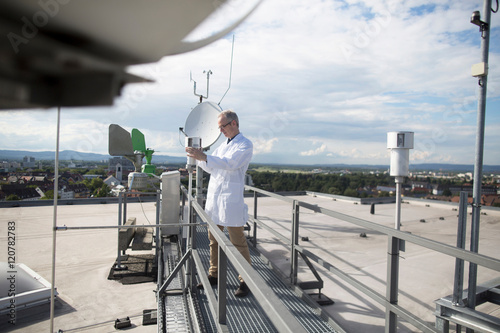 Male meteorologist updating meteorological equipment measurements at rooftop weather station