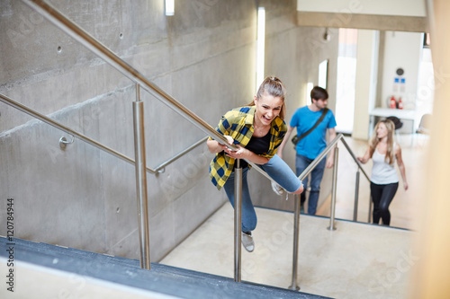 Young female student sliding down stairway handrail at higher education college photo