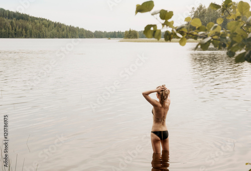 Rear view of woman with hands in hair in lake, Orivesi, Finland photo