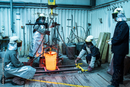 Male foundry workers winching bronze melting pot in bronze foundry
