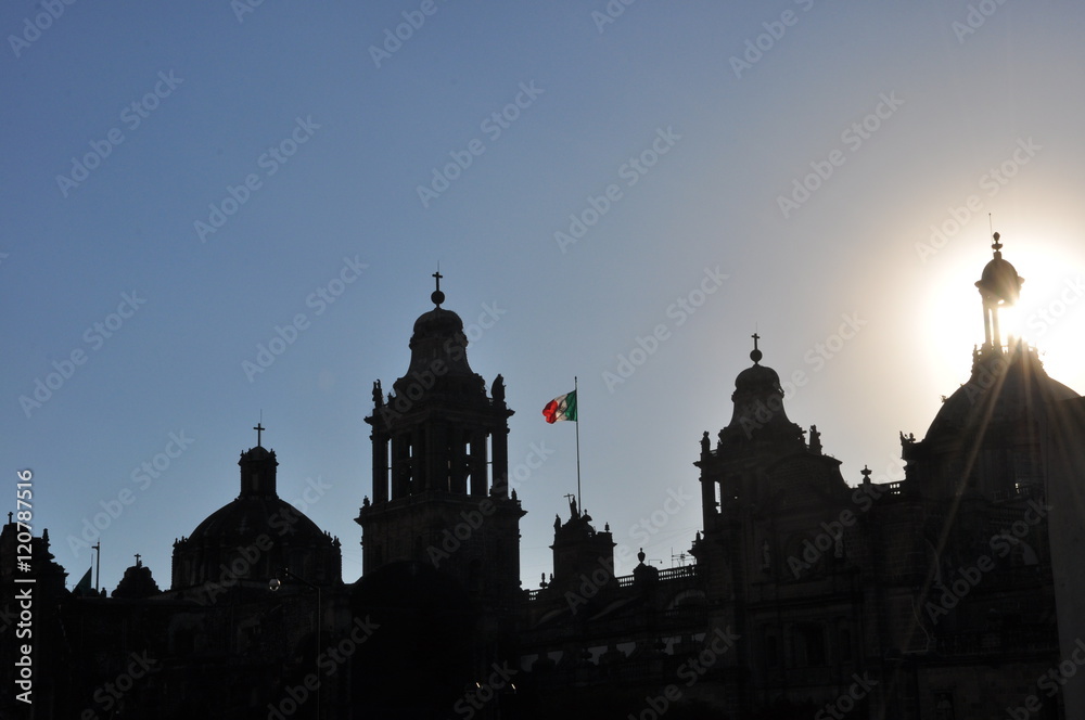 Mexican flag waiving behind silhouetted buildings in El Zocalo, Mexico City