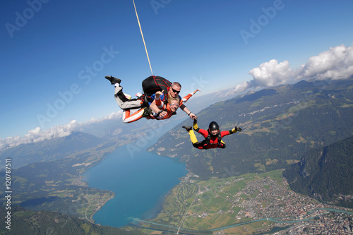 Smiling tandem sky divers holding hand with free faller, Interlaken, Berne, Switzerland photo