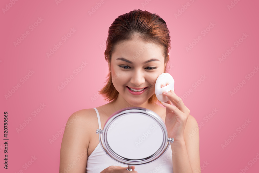 Young lady applying blusher on her face with powder puff and mir Young lady applying blusher on her face with powder puff and mir