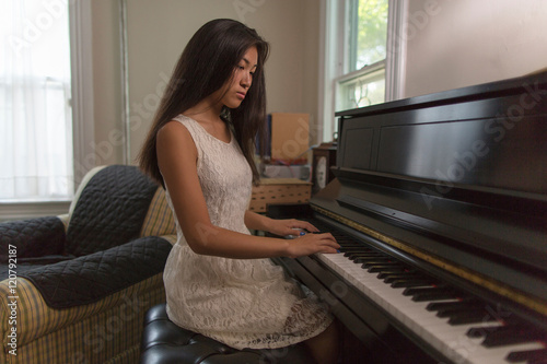 Teenage girl sitting playing piano in dining room