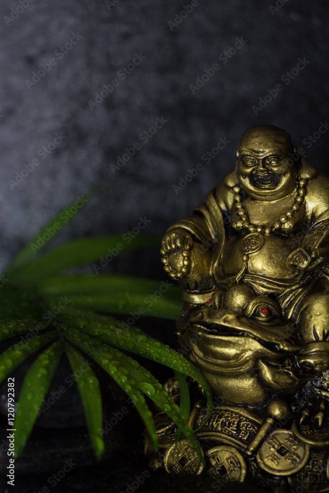 Wet Laughing Buddha with black basalt stones and green leaf, on black background Wet Laughing Buddha with black basalt stones and green leaf, on black background