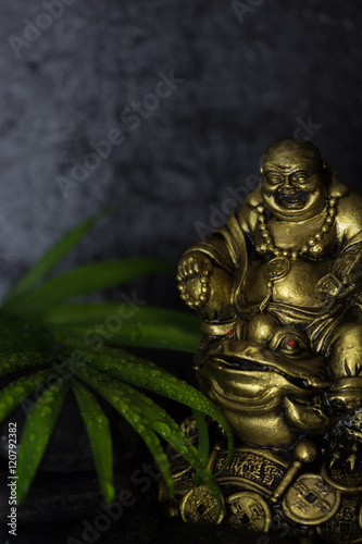Wet Laughing Buddha with black basalt stones and  green leaf, on black background © okolaa