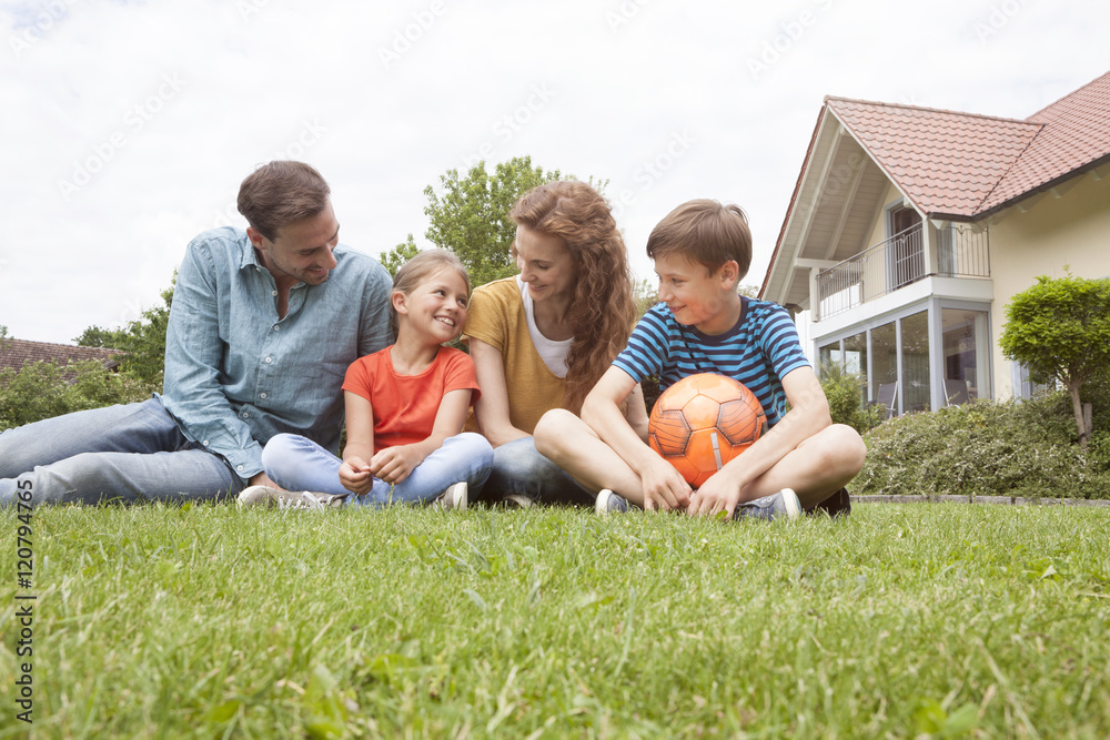 Smiling family sitting in garden with football Smiling family sitting in garden with football
