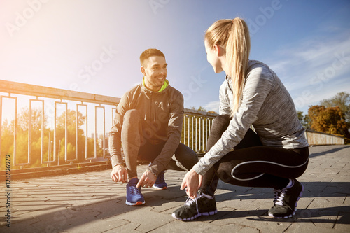 smiling couple tying shoelaces outdoors