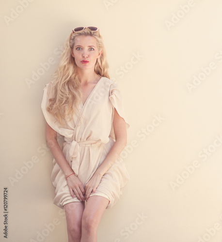Summer portrait of young beautiful blond woman in white dress posing near the wall and have fun. Toned in warm colors
