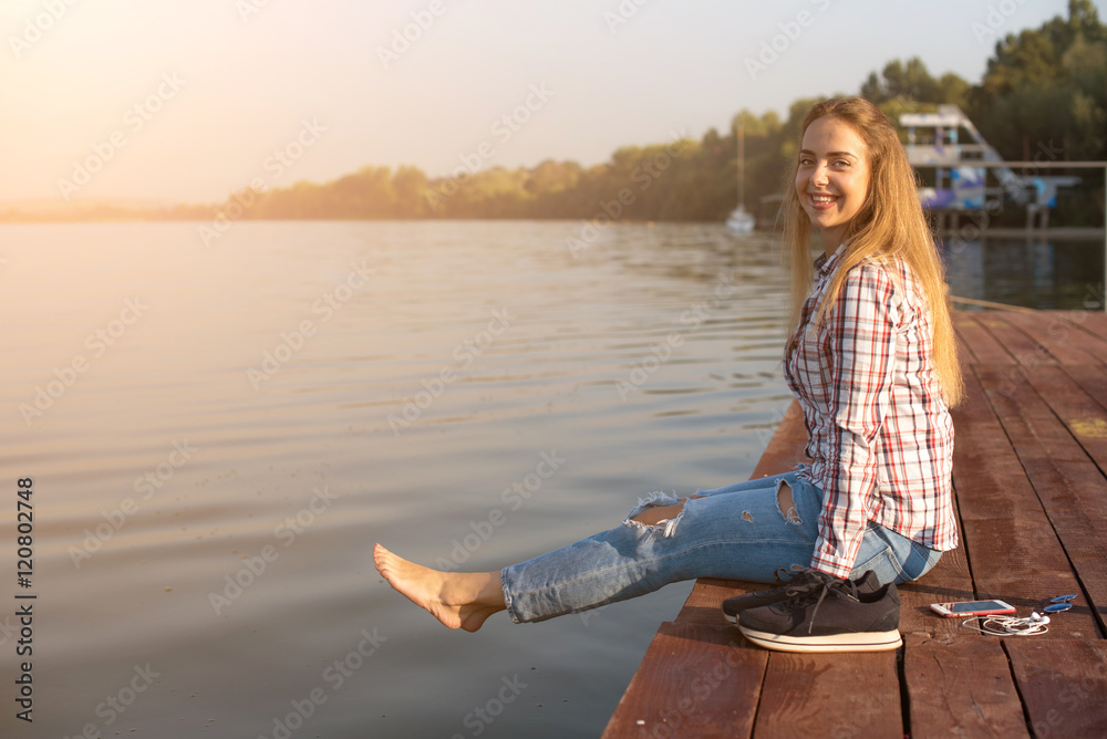 Fototapeta premium Beautiful young girl resting on a pier near the water at dawn
