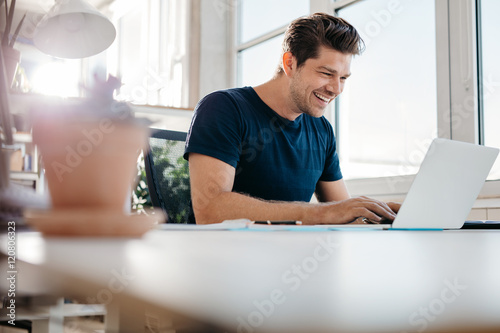 Happy young businessman using laptop at his office desk