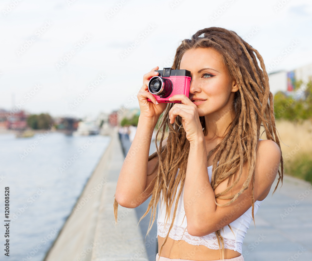Portrait of Trendy Girl with Dreads and Vintage Camera Standing by the River. Modern Youth Lifestyle Concept. Take the picture.