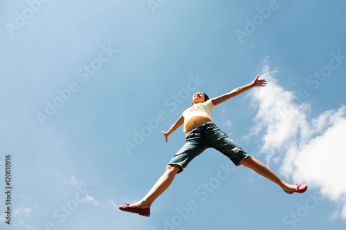 View from below of leaping happy girl on the background of blue sky