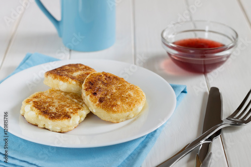 Cottage cheese pancakes with cranberry sauce on white wooden tab