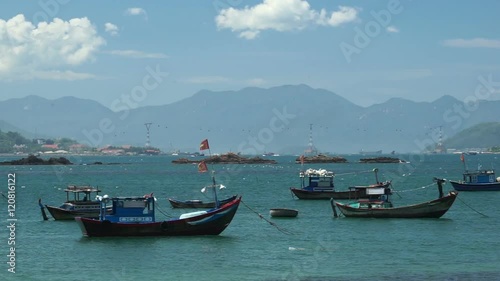 Few fishing boats are shaking on water at the local vietnamese river. Summer sunny windy day. Mountains behind. photo