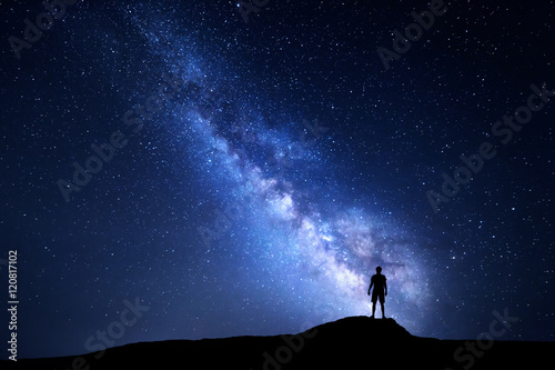 Milky Way. Beautiful night sky with stars and silhouette of a standing alone man on the mountain. Blue milky way with man on the hill. Background with galaxy and silhouette of a man. Universe photo