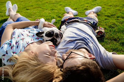 Couple lying with French bulldog on grass in park.