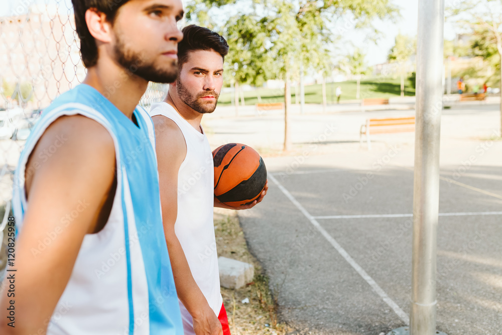 Portrait of two friends relaxing after playing basketball on court.