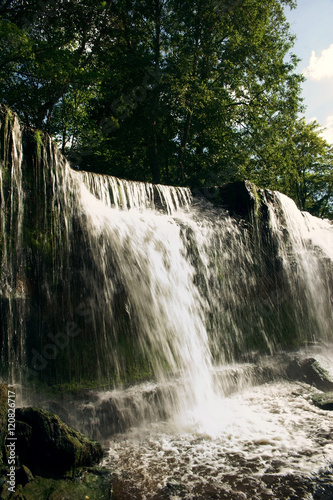 Flowing waterfall in green forest on a summer sunny day