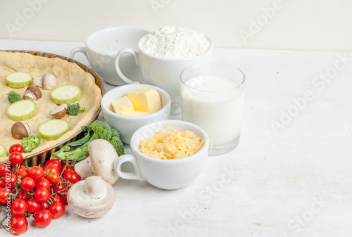 The selection of ingredients for the preparation of traditional French dishes quiche lorraine  on white wooden table with a baked dough in the baking dish in the cooking process  copy space