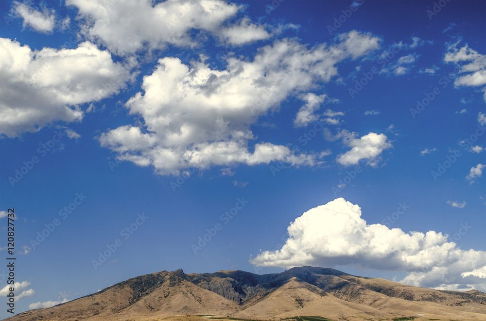 Mount Aragats in sunny day against the blue sky covered by clouds