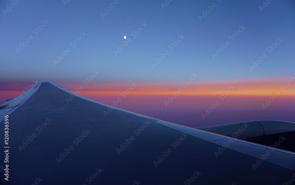 A pink and blue sky with the moon over an airplane wing