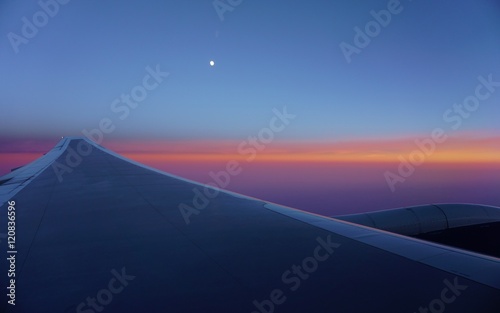 A pink and blue sky with the moon over an airplane wing © eqroy