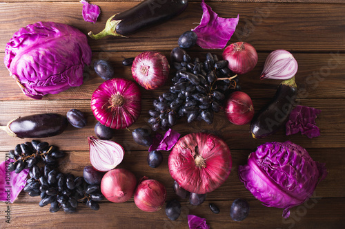 Purple fruits and vegetables. Blue onion, purple cabbage, eggplant, grapes and plums on a wooden background.