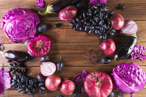 Purple fruits and vegetables. Blue onion, purple cabbage, eggplant, grapes and plums on a wooden background.
