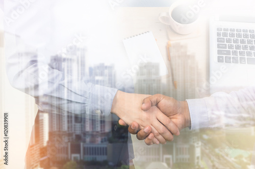 Businessman handshake on the city and office desk background