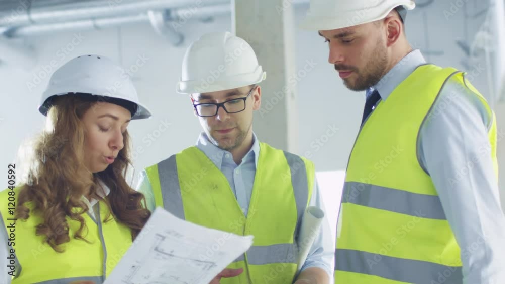 Team of Engineers in Hard Hats Having Conversation, Looking at Blueprint, inside Building Under Construction. Shot on RED Cinema Camera in 4K (UHD). Team of Engineers in Hard Hats Having Conversation, Looking at Blueprint, inside Building Under Construction. Shot on RED Cinema Camera in 4K (UHD).