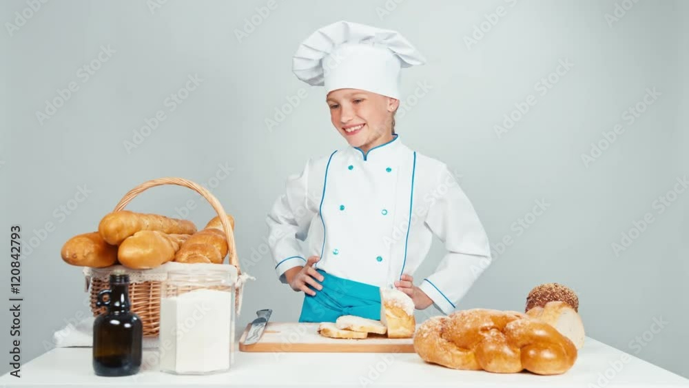 Baker girl standing near kitchen table with bakery products and smiling at camera. Thumbs up. OK Baker girl standing near kitchen table with bakery products and smiling at camera. Thumbs up. OK