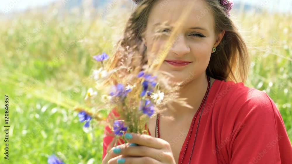 Girl with wreath of flowers sitting on the field and looking to the camera, steadycam shot
