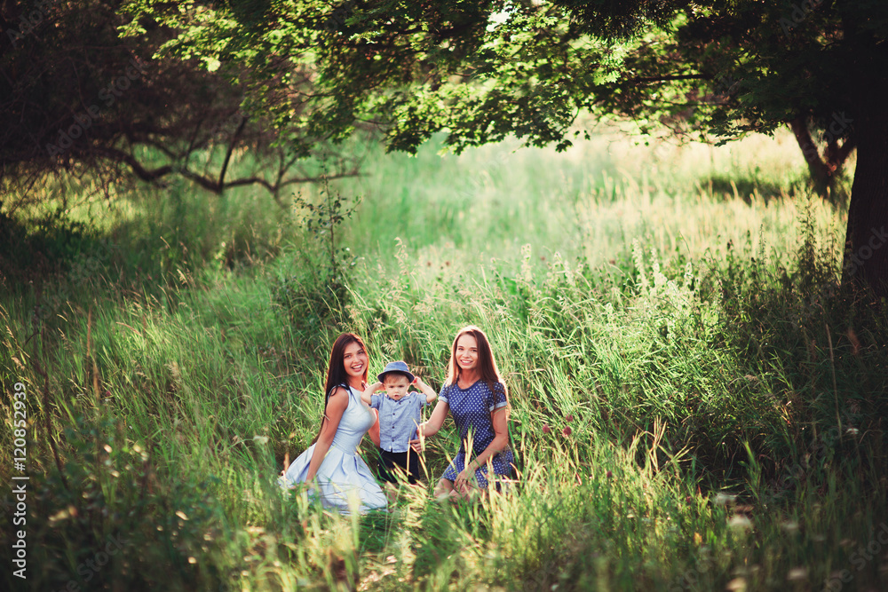 Beautiful happy family resting in nature. Two women - mom and aunt play with a boy in the Park. soft focus