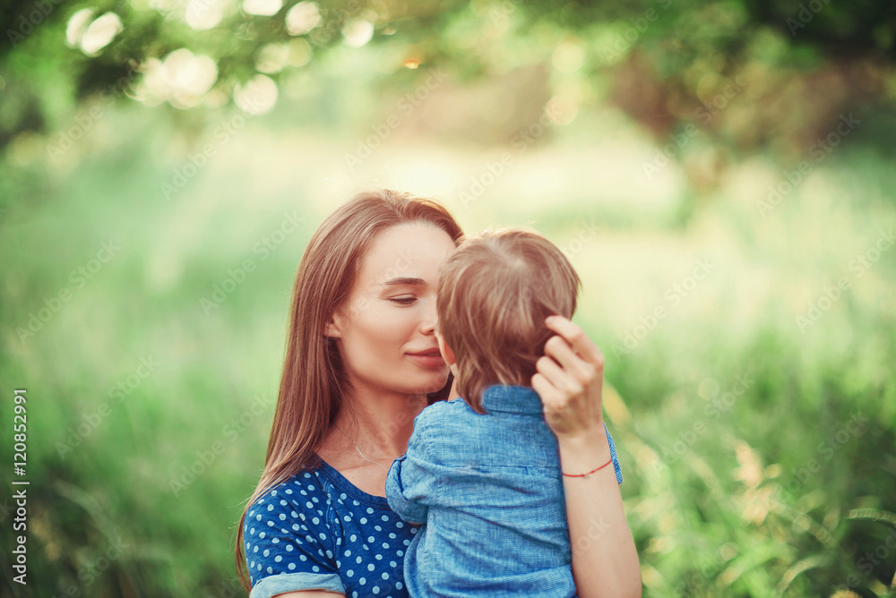 Loving mother holding son in her arms, plays with him and hugs him. Family rest on the nature. soft focus