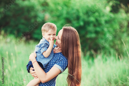 Loving mother holding son in her arms, plays with him and hugs him. Family rest on the nature. soft focus