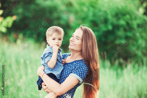 Loving mother holding son in her arms, plays with him and hugs him. Family rest on the nature. soft focus
