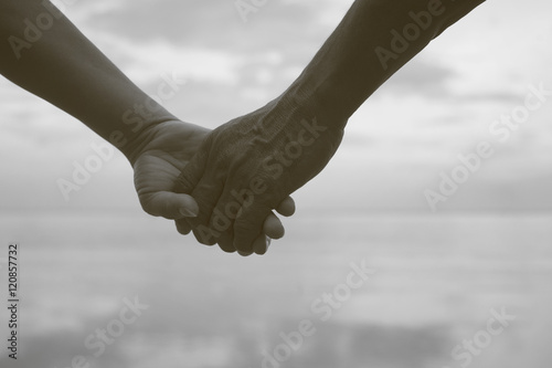 close up hand of senior couple holding hand together near seaside at the beach,black and white picture color,filtered image,light effect added,selective focus,love forever concept