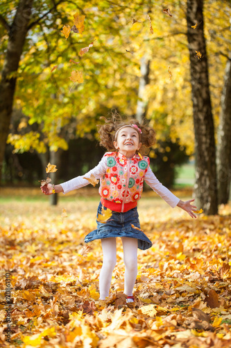 Young girl throwing leaves in autumn park