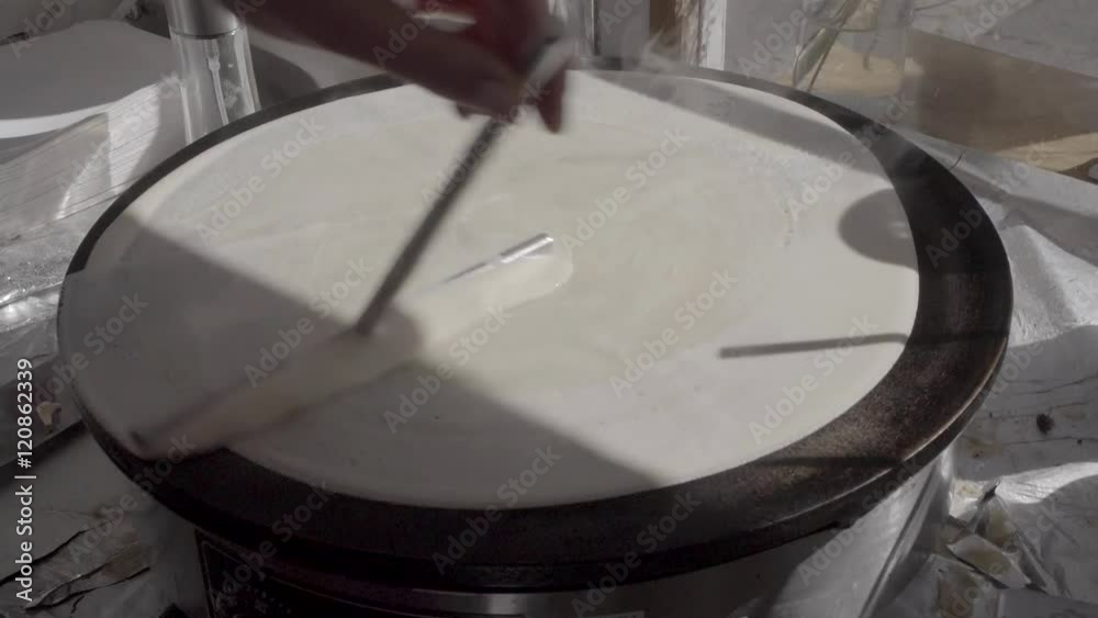 Dough on crepes / pancake maker being spread by T-shaped stick. SLOG3, medium shot.