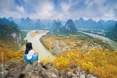 Chinesse woman sitting on the top of mountain and enjoing view on valley with rocks. Xing Ping, Yangshuo, China. photo