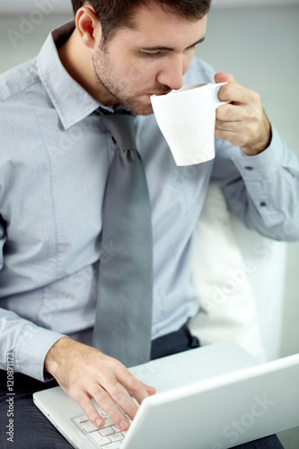 Businessman drinking coffee and typing on laptop