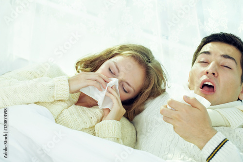 Young couple sneezing and blowing their noses