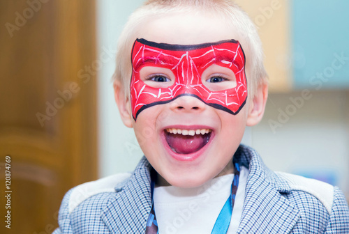 Spiderboy.
Excited caucasian boy with a spiderman mask on his face smiles at camera.
