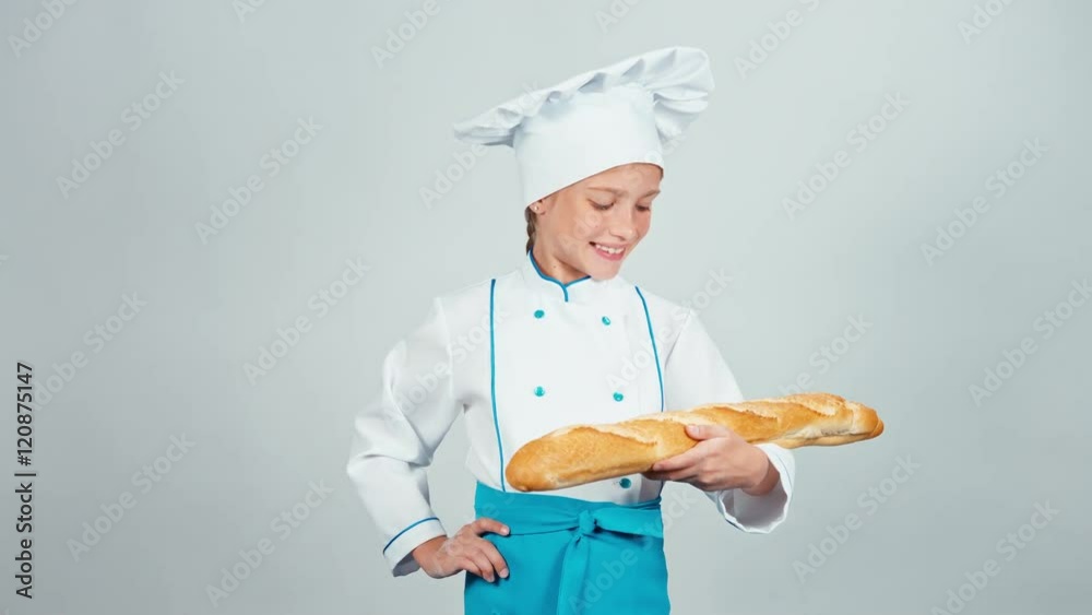 Baker girl 7-8 years child holds bread baguette and gives you it at camera and smiling Baker girl 7-8 years child holds bread baguette and gives you it at camera and smiling