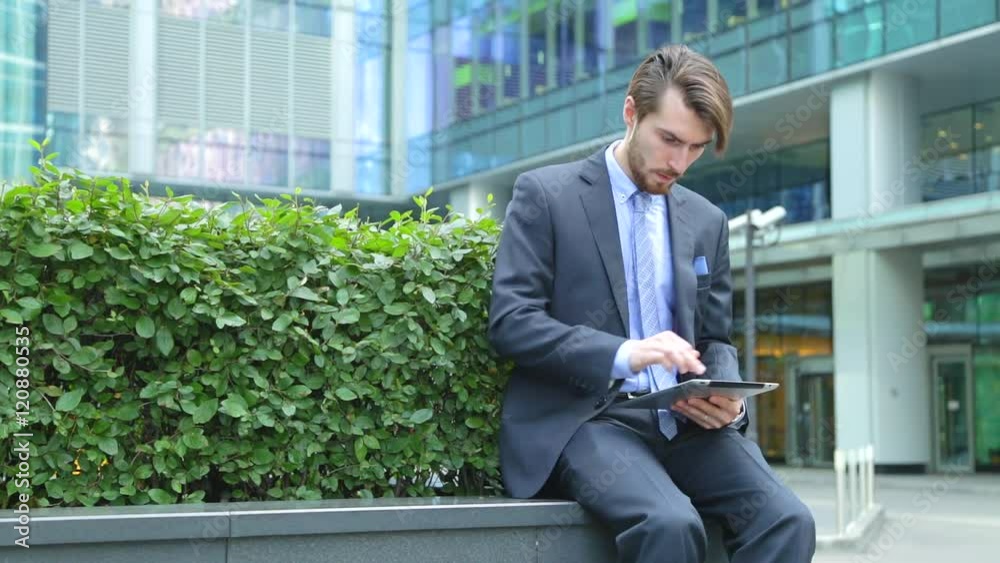 Handsome businessman is using tablet computer near the modern business center, skyscraper Handsome businessman is using tablet computer near the modern business center, skyscraper