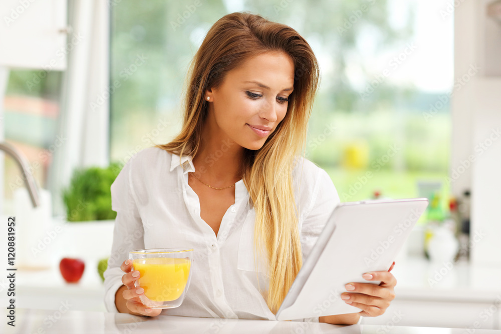 Young woman with orange juice and tablet in kitchen Young woman with orange juice and tablet in kitchen